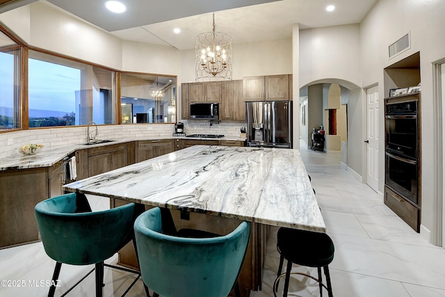 kitchen featuring arched walkways, stainless steel appliances, visible vents, decorative backsplash, and a sink