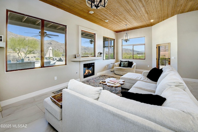 living area with recessed lighting, ceiling fan with notable chandelier, wood ceiling, baseboards, and a glass covered fireplace