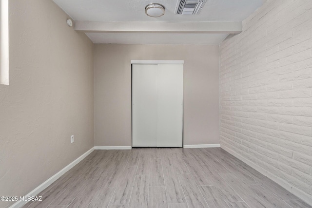 empty room with beamed ceiling, brick wall, and light wood-type flooring