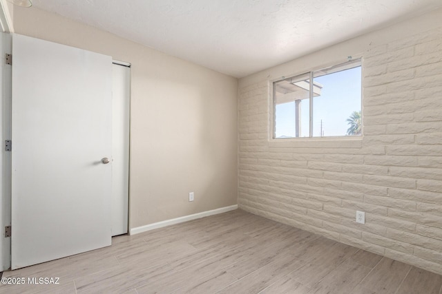 spare room featuring brick wall and light wood-type flooring