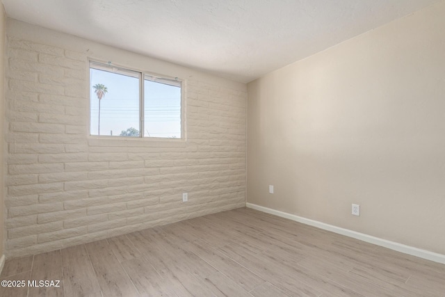 spare room featuring brick wall and light wood-type flooring