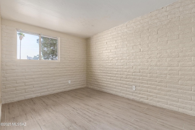 spare room featuring brick wall and light hardwood / wood-style floors