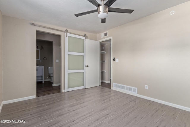 unfurnished bedroom featuring ceiling fan, a barn door, and a closet