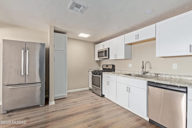 kitchen with sink, appliances with stainless steel finishes, white cabinetry, light hardwood / wood-style floors, and light stone countertops