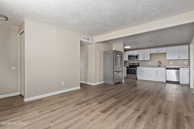 kitchen featuring stainless steel appliances, light hardwood / wood-style floors, a textured ceiling, and white cabinets