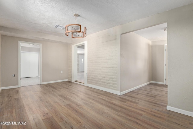 unfurnished room featuring an inviting chandelier, hardwood / wood-style flooring, and a textured ceiling