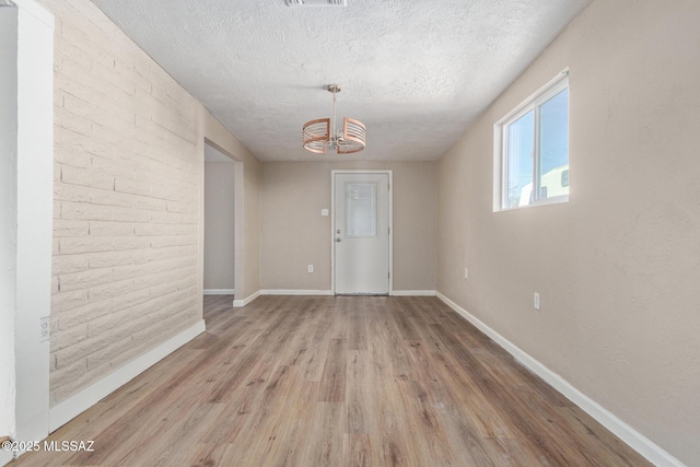 spare room with light hardwood / wood-style floors, a textured ceiling, and a notable chandelier