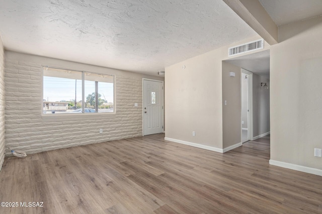 empty room featuring wood-type flooring, brick wall, and a textured ceiling