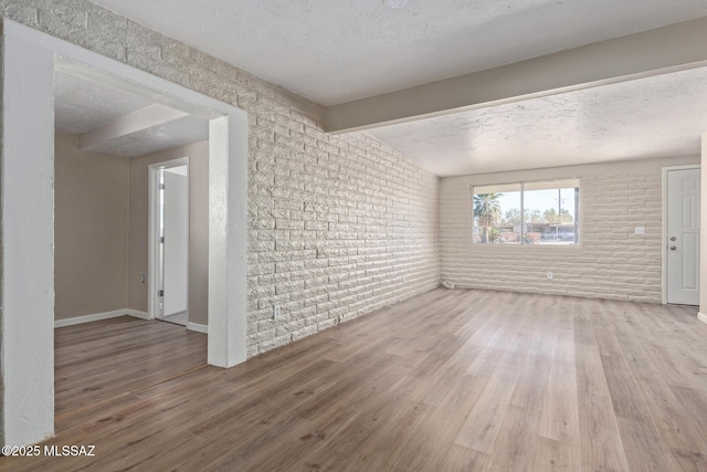 spare room featuring hardwood / wood-style flooring, brick wall, lofted ceiling with beams, and a textured ceiling