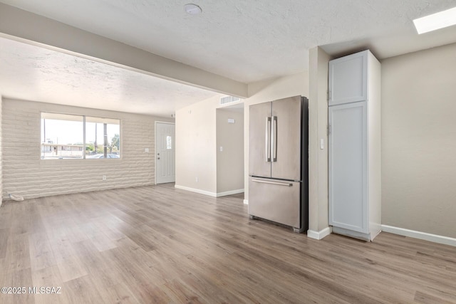 unfurnished living room with brick wall, light hardwood / wood-style flooring, and a textured ceiling