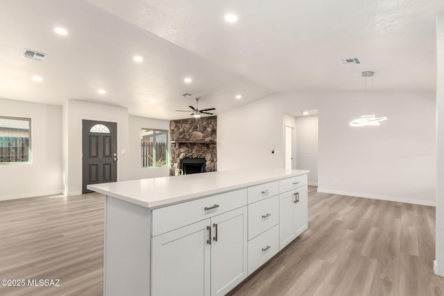 kitchen featuring a stone fireplace, white cabinetry, hanging light fixtures, ceiling fan, and light hardwood / wood-style flooring