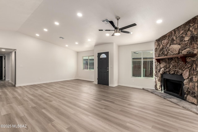 unfurnished living room featuring a stone fireplace, lofted ceiling, ceiling fan, and light hardwood / wood-style flooring