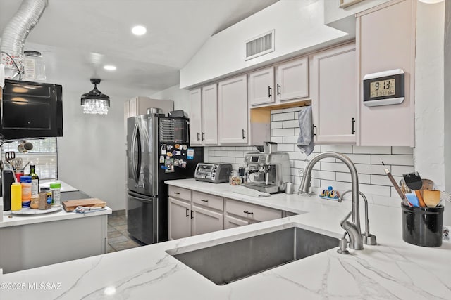 kitchen with sink, light stone counters, stainless steel refrigerator, pendant lighting, and backsplash