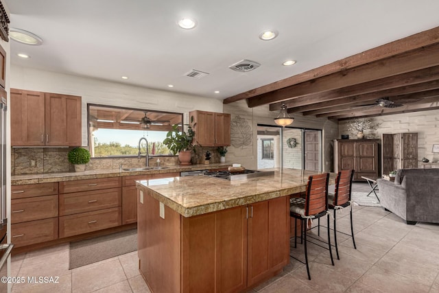 kitchen featuring a kitchen island, sink, a breakfast bar area, stainless steel gas cooktop, and beam ceiling