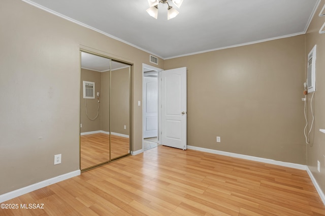 unfurnished bedroom featuring a wall mounted air conditioner, crown molding, light hardwood / wood-style flooring, and a closet