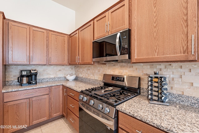 kitchen with light stone countertops, appliances with stainless steel finishes, light tile patterned floors, and backsplash