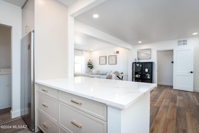 kitchen featuring a peninsula, visible vents, open floor plan, and wood finished floors