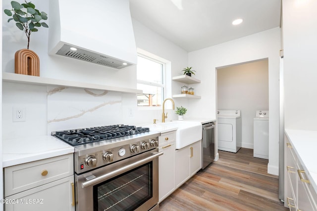 kitchen featuring light wood finished floors, washer and clothes dryer, appliances with stainless steel finishes, premium range hood, and open shelves