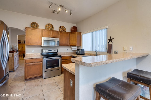 kitchen with appliances with stainless steel finishes, a breakfast bar, sink, light tile patterned floors, and kitchen peninsula