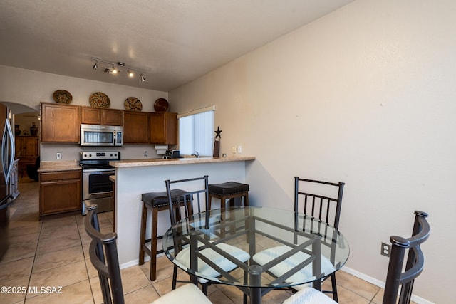 kitchen featuring light tile patterned floors, a breakfast bar, kitchen peninsula, and appliances with stainless steel finishes