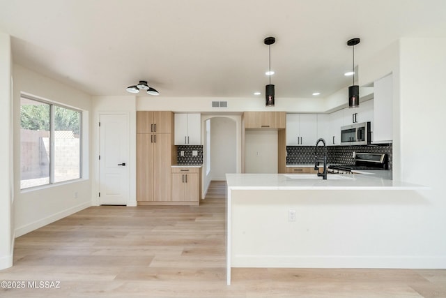 kitchen featuring pendant lighting, appliances with stainless steel finishes, light brown cabinets, decorative backsplash, and light wood-type flooring