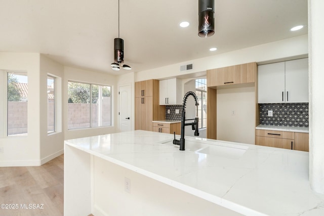 kitchen featuring sink, white cabinetry, tasteful backsplash, decorative light fixtures, and light stone countertops