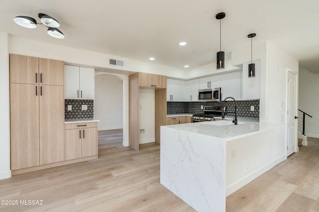 kitchen with appliances with stainless steel finishes, pendant lighting, white cabinets, and light stone counters