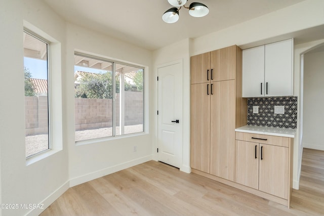 kitchen with a chandelier, light brown cabinetry, light hardwood / wood-style floors, and decorative backsplash