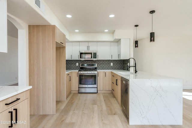 kitchen with sink, appliances with stainless steel finishes, white cabinetry, light stone counters, and kitchen peninsula