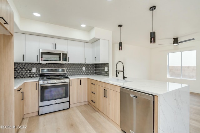 kitchen with sink, white cabinetry, kitchen peninsula, pendant lighting, and stainless steel appliances