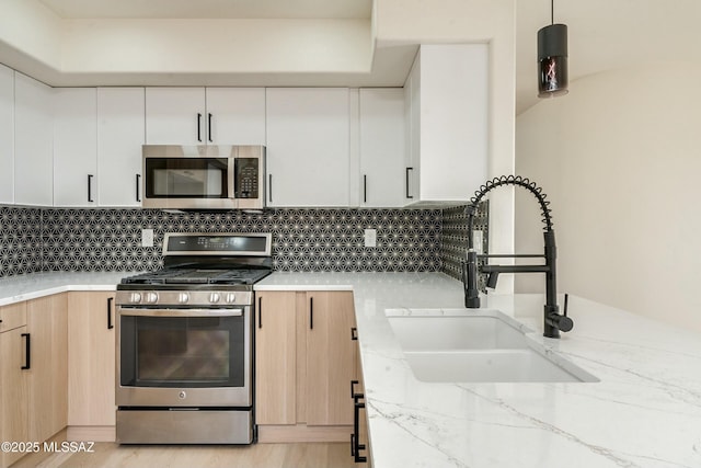 kitchen with sink, white cabinetry, light brown cabinets, appliances with stainless steel finishes, and pendant lighting