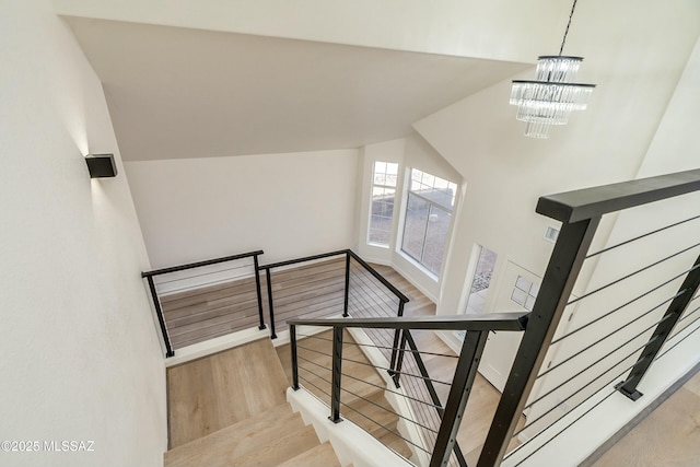 stairs featuring hardwood / wood-style flooring, vaulted ceiling, and a notable chandelier