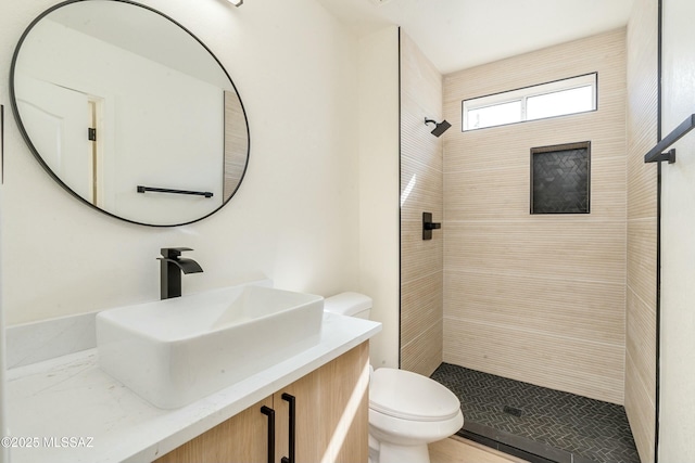 bathroom featuring vanity, a tile shower, and toilet