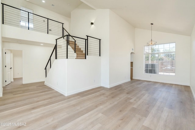 unfurnished living room featuring a towering ceiling, a chandelier, and light wood-type flooring