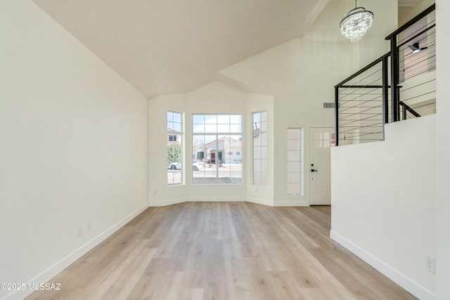 unfurnished living room with high vaulted ceiling, an inviting chandelier, and light hardwood / wood-style floors