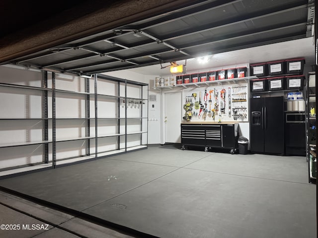 garage with a garage door opener, black refrigerator with ice dispenser, and a workshop area