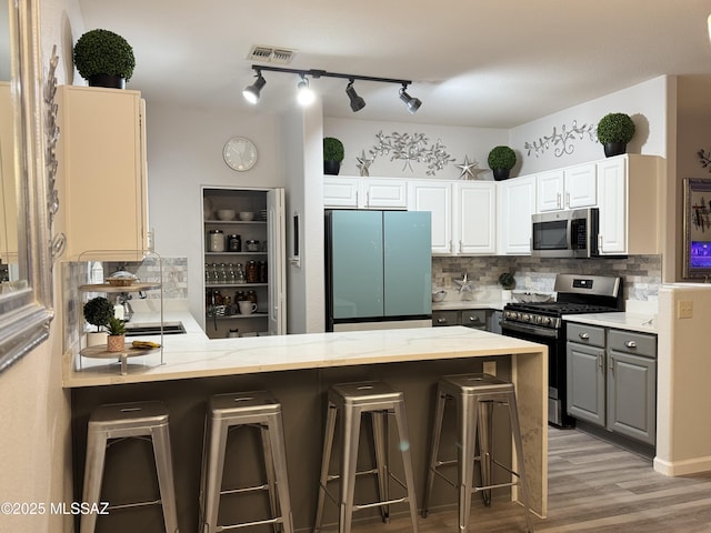 kitchen with a kitchen bar, white cabinetry, kitchen peninsula, stainless steel appliances, and decorative backsplash