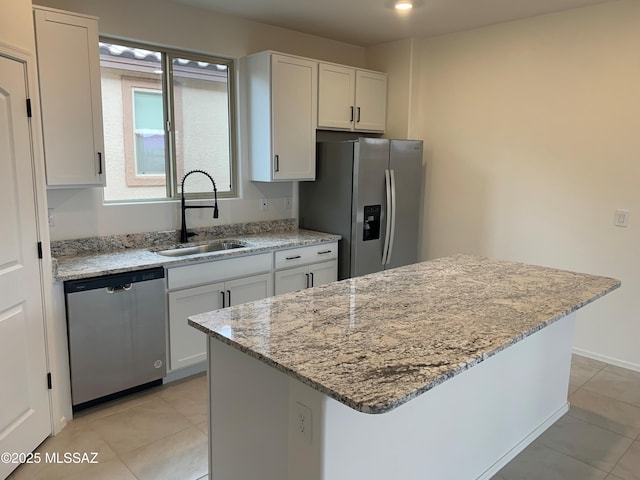 kitchen with sink, appliances with stainless steel finishes, a kitchen island, light stone countertops, and white cabinets