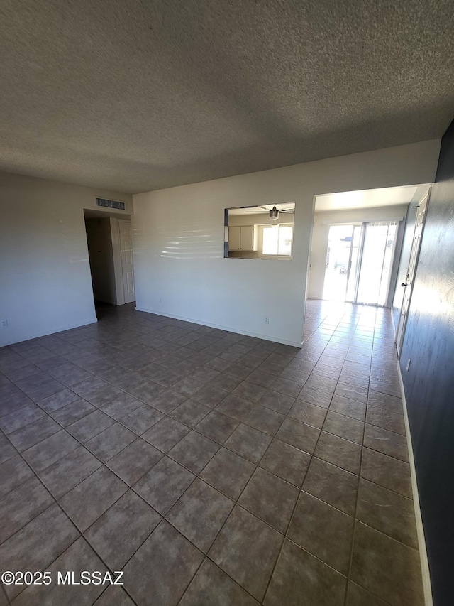 empty room featuring ceiling fan, dark tile patterned flooring, and a textured ceiling