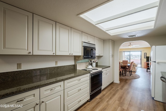 kitchen with light hardwood / wood-style flooring, a skylight, black appliances, white cabinets, and dark stone counters