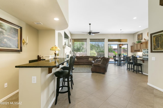kitchen with a breakfast bar, sink, dark stone countertops, hanging light fixtures, and ceiling fan