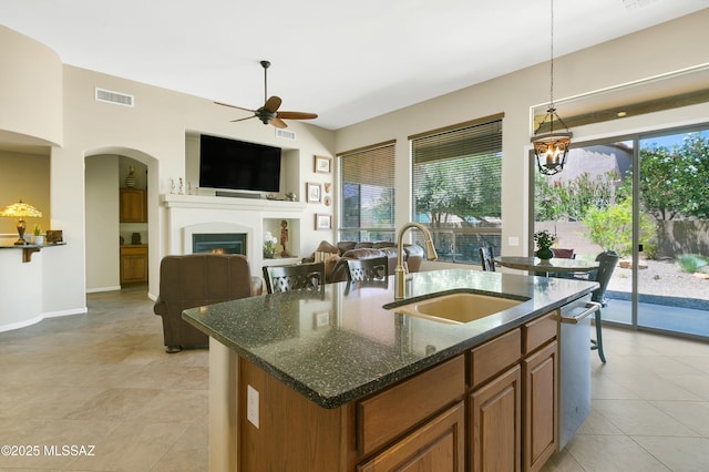 kitchen with sink, ceiling fan, dark stone countertops, an island with sink, and decorative light fixtures