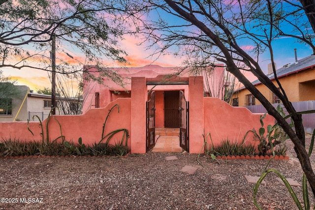 pueblo-style house featuring a fenced front yard, a gate, and stucco siding