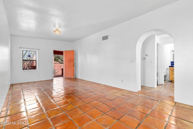 empty room featuring arched walkways, light tile patterned floors, and visible vents