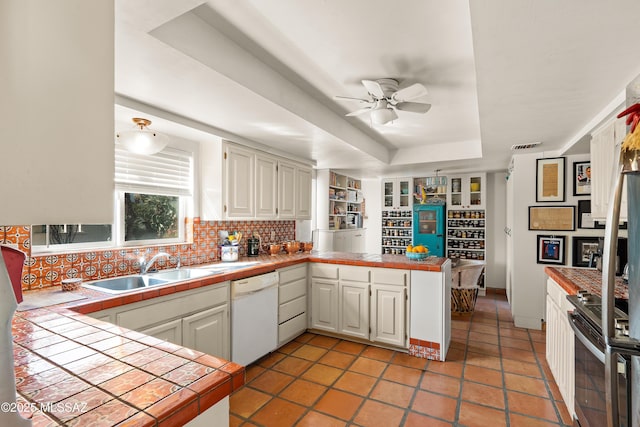 kitchen with white cabinets, tile counters, white dishwasher, kitchen peninsula, and a raised ceiling