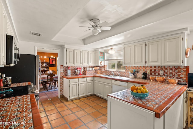 kitchen featuring dishwasher, tasteful backsplash, a tray ceiling, tile counters, and white cabinets