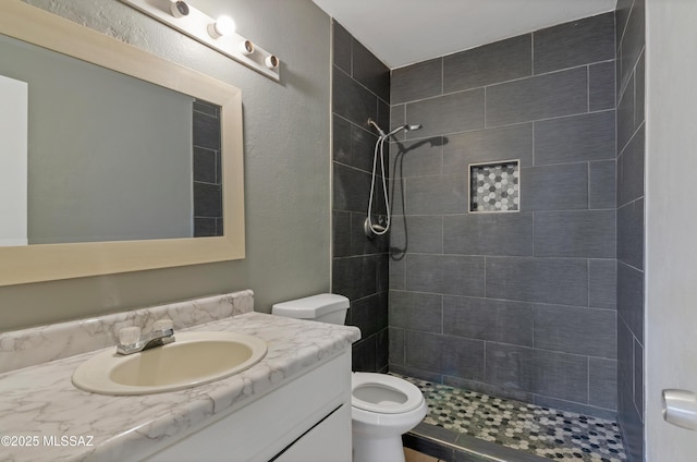 bathroom featuring a tile shower, vanity, and toilet