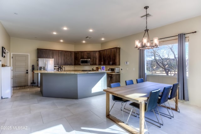 kitchen featuring decorative light fixtures, an island with sink, decorative backsplash, dark brown cabinetry, and stainless steel appliances