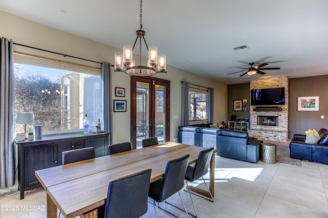 tiled dining room with french doors, a fireplace, and ceiling fan with notable chandelier