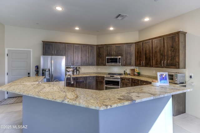 kitchen with appliances with stainless steel finishes, dark brown cabinets, backsplash, and light stone counters